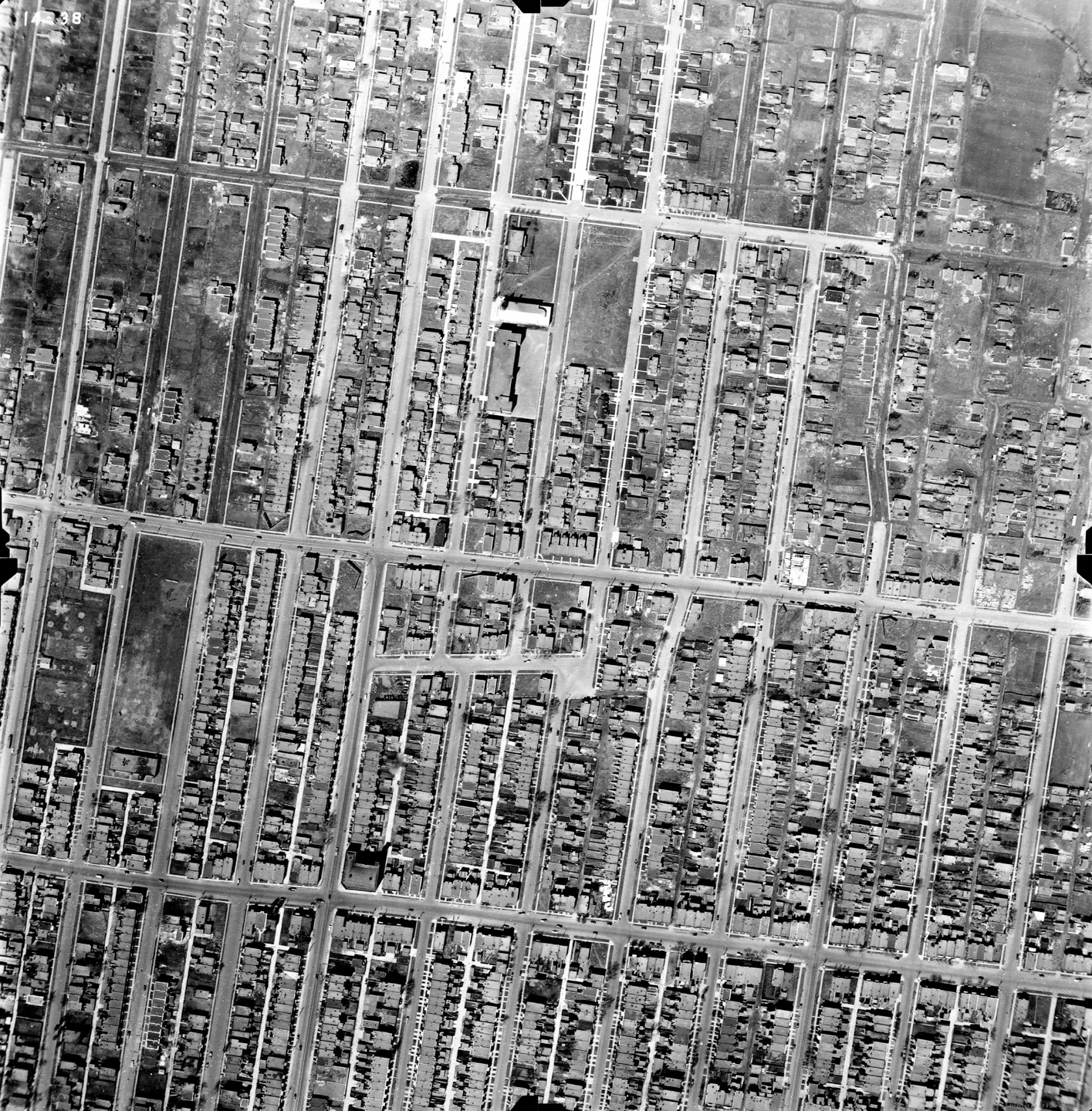 Rue en noir et blanc avec des bâtiments, un parc en arrière‑plan et plusieurs voitures garées