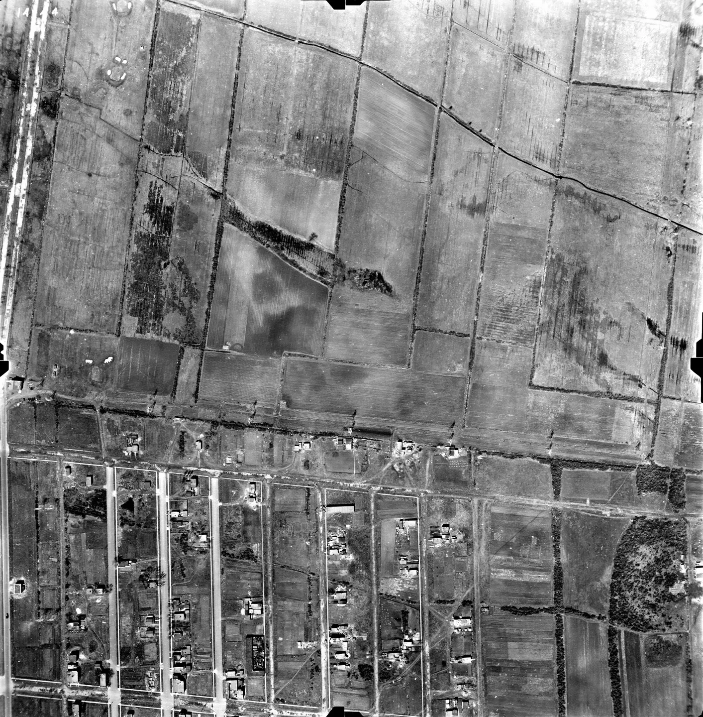 Photo en noir et blanc d’une zone rurale de Saint‑Léonard avec un grand champ et quelques maisons.