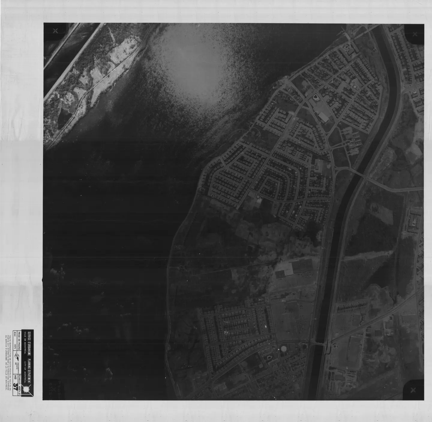 Photo en noir et blanc d’un bâtiment urbain près d’un plan d’eau, des voitures garées, vue aérienne