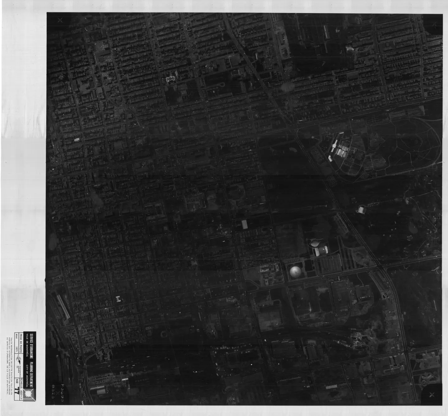 Photo en noir et blanc d'une rue avec bâtiments, un parc et un stade