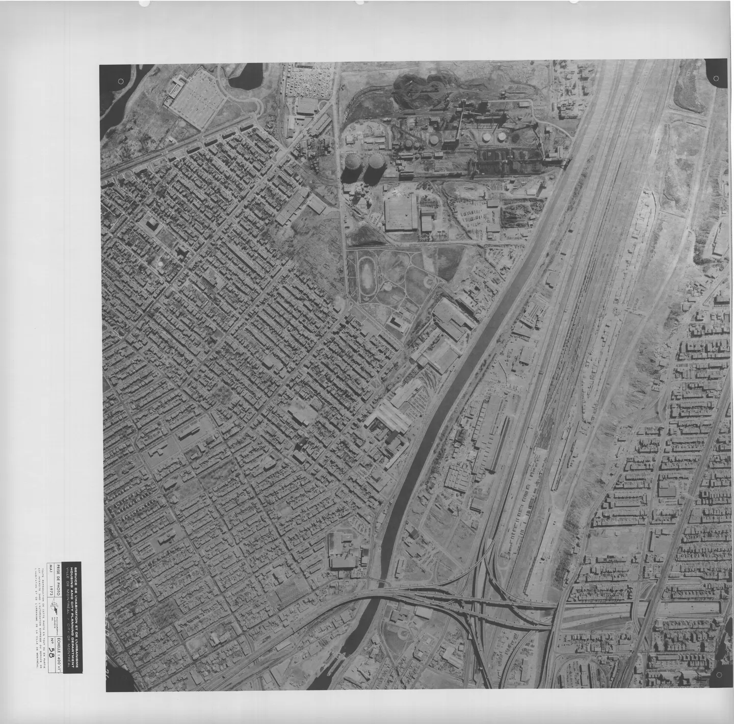 Vue aérienne d'une rue de Montréal avec des bâtiments, des voitures garées, un parc et une autoroute.