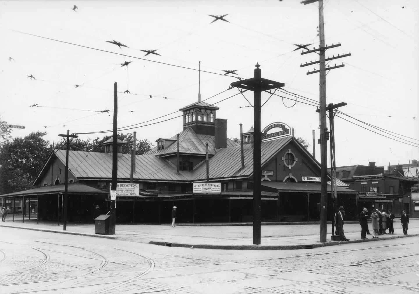 Photo en noir et blanc d'un bâtiment bas avec une tour centrale à une intersection, câbles au-dessus.