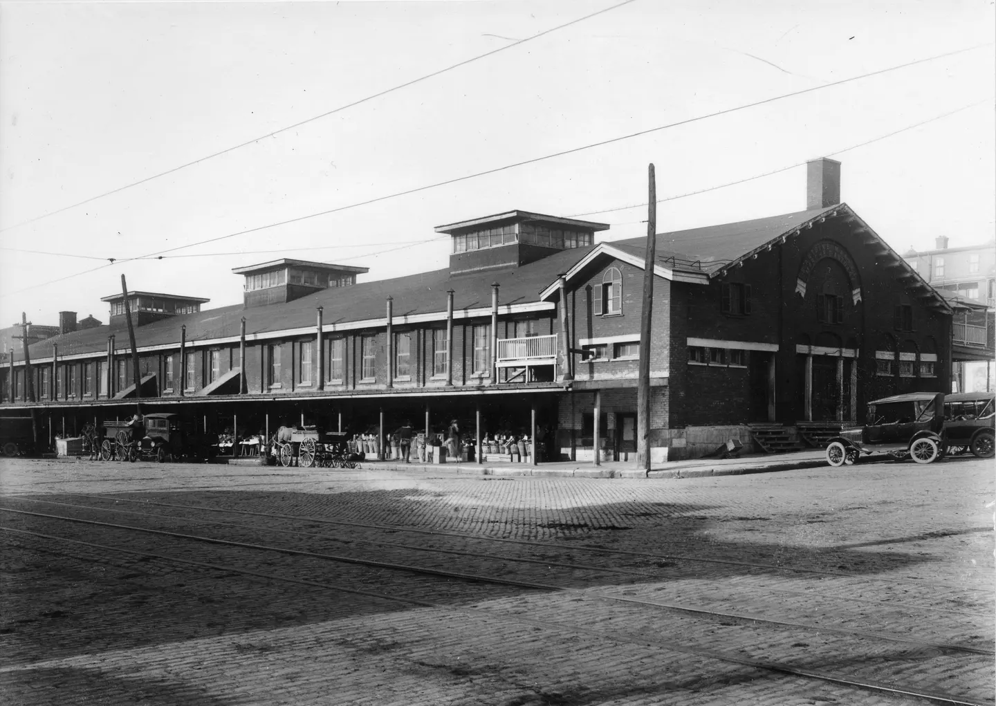 Photo en noir et blanc d'un bâtiment à l'architecture des années 1920, tour de l'horloge, piétons, voiture