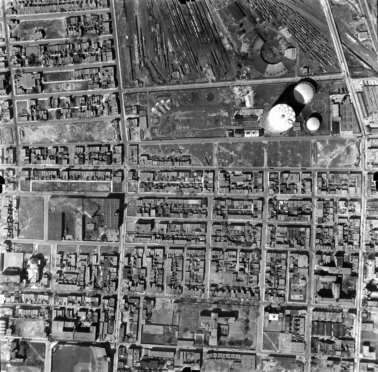 Black‑and‑white photo of a city with tall buildings, a central dome, cars and pedestrians