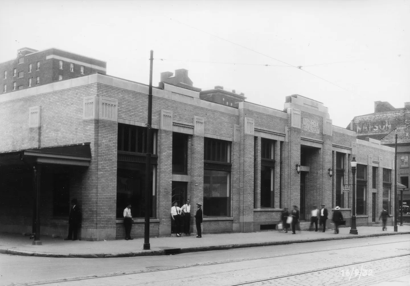Groupe de personnes sur trottoir, bâtiment à l'arrière, style 1930s, accessoires visibles